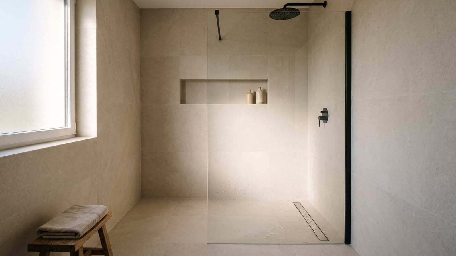 Douche à l'italienne de plain-pied en grès cérame grand format ton pierre, avec caniveau linéaire le long du mur, paroi en verre fixe et niche murale